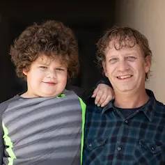 Boy with curly hair standing with arm on Dad's shoulder