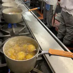 Potatoes boiling on the stove with culinary students working at table nearby
