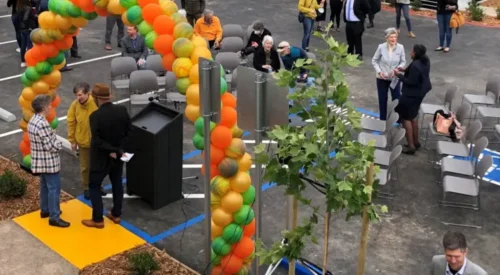 people gathered under an arch of orange and green balloons