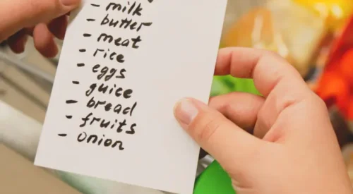 Person holds a shopping list with list of groceries