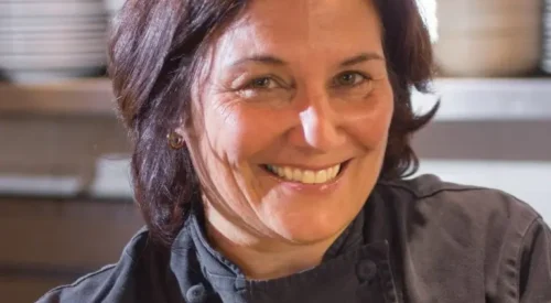 Dark-haired woman in black chef coat smiles at the camera