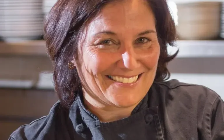 Dark-haired woman in black chef coat smiles at the camera