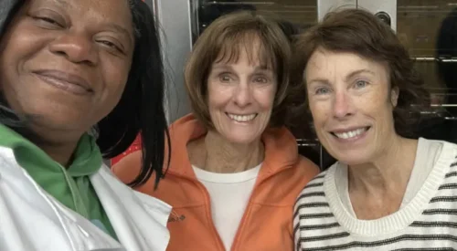 Cook in white culinary jacket smiles arm in arm with two women volunteers