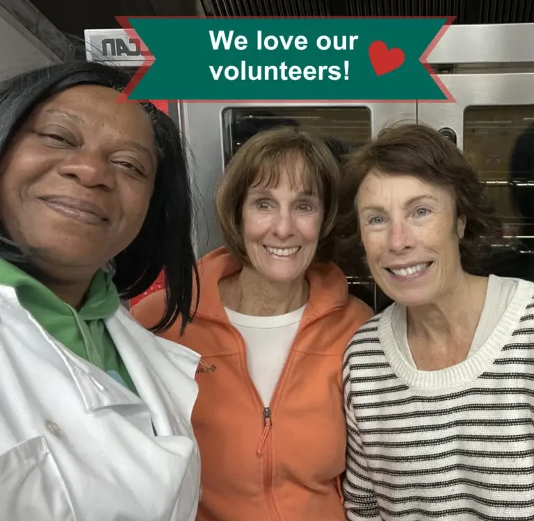 Cook in white culinary jacket smiles arm in arm with two women volunteers
