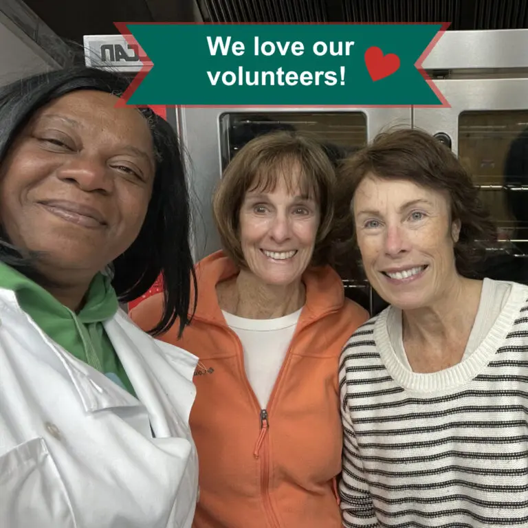 Cook in white culinary jacket smiles arm in arm with two women volunteers