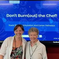 Two woman standing in front of poster "don't burnout the chef"