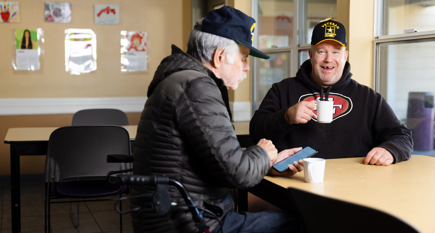 Two veterans sit at a table talking and drinking from coffee cups