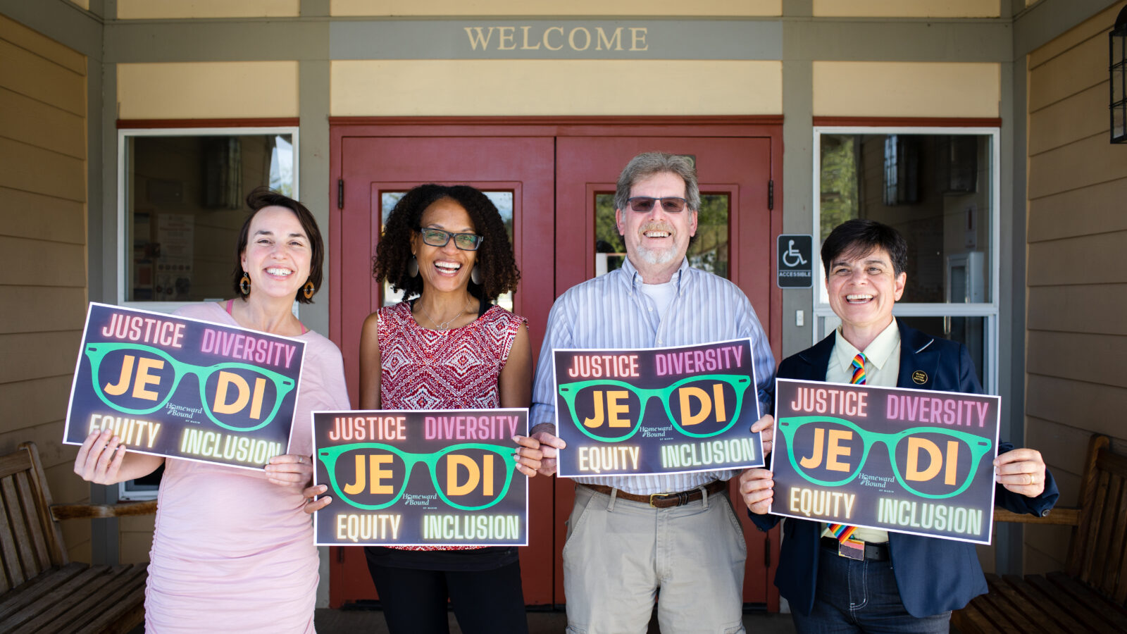 Four people standing in front of a building holding signs that read: JEDI