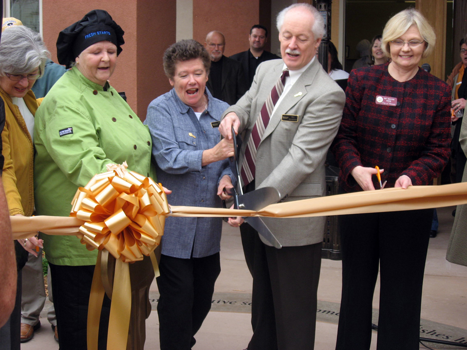 4 people stand behind a ribbon, cutting it with a pair of scissors