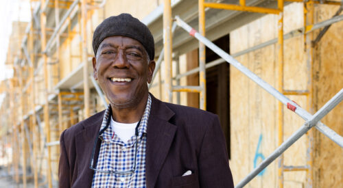 A man stands in front of a construction site with his hands in his pockets