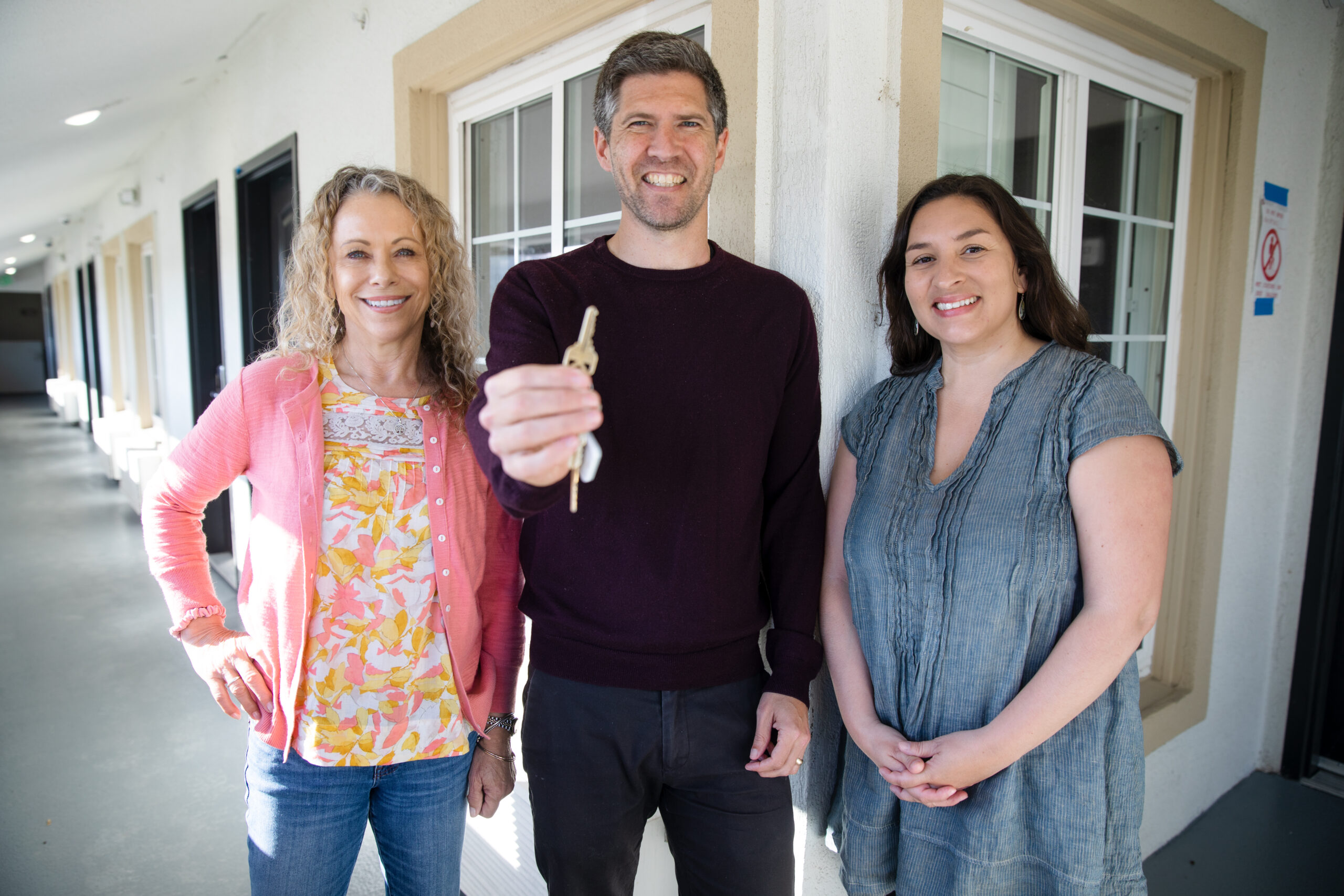 A man shows his new key with a woman standing on either side of him.