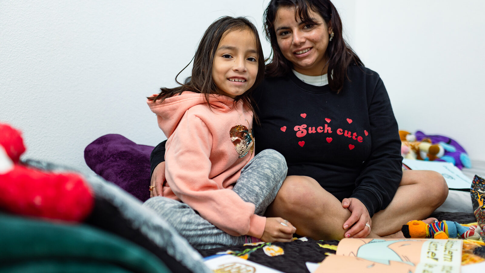 A mother and her daughter sit on a bed looking proudly at the camera