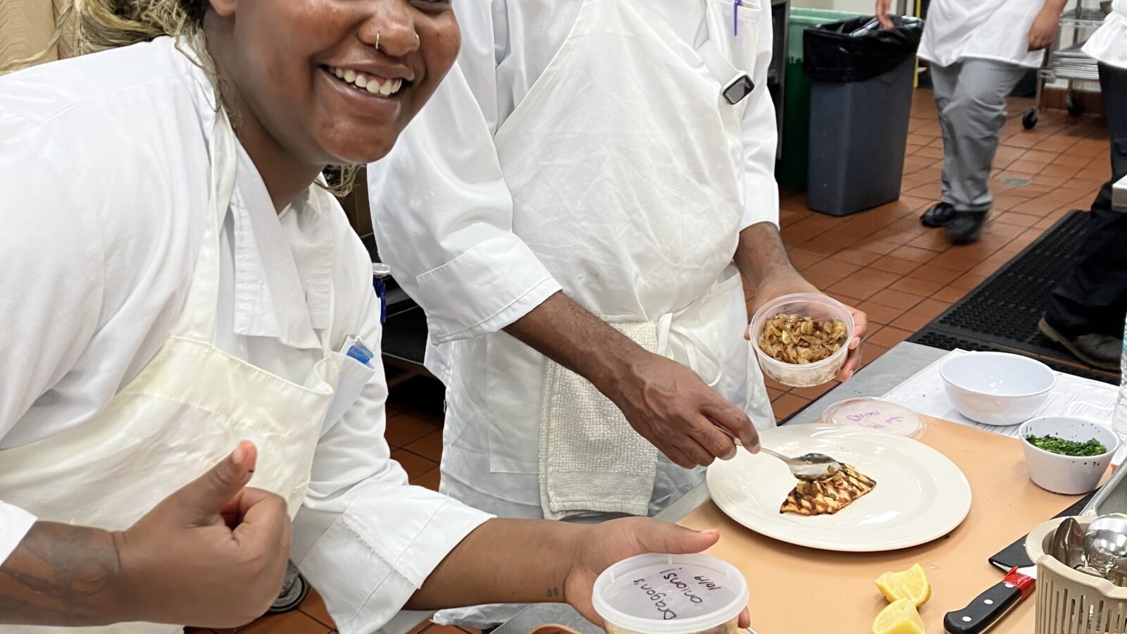 Two chefs in the Fresh Starts Culinary Academy prepare plates of food