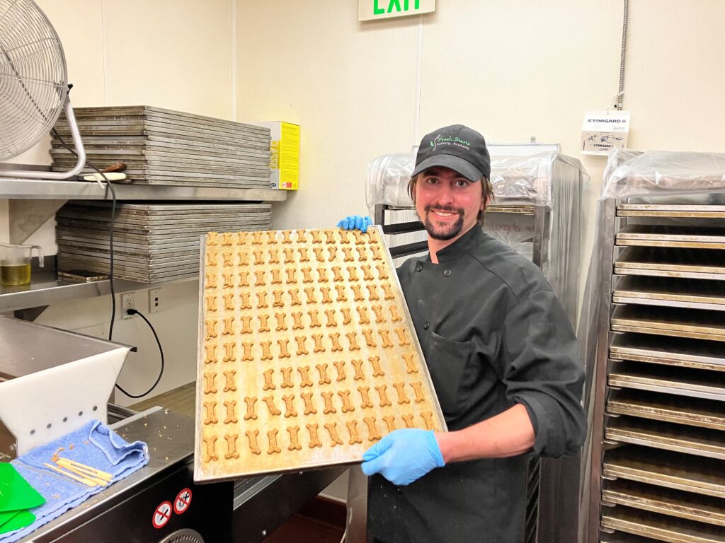 a man in a chef uniform holding a baking sheet of dog treats
