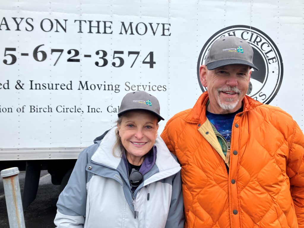 Marsha and Greg smiling in front of a moving truck