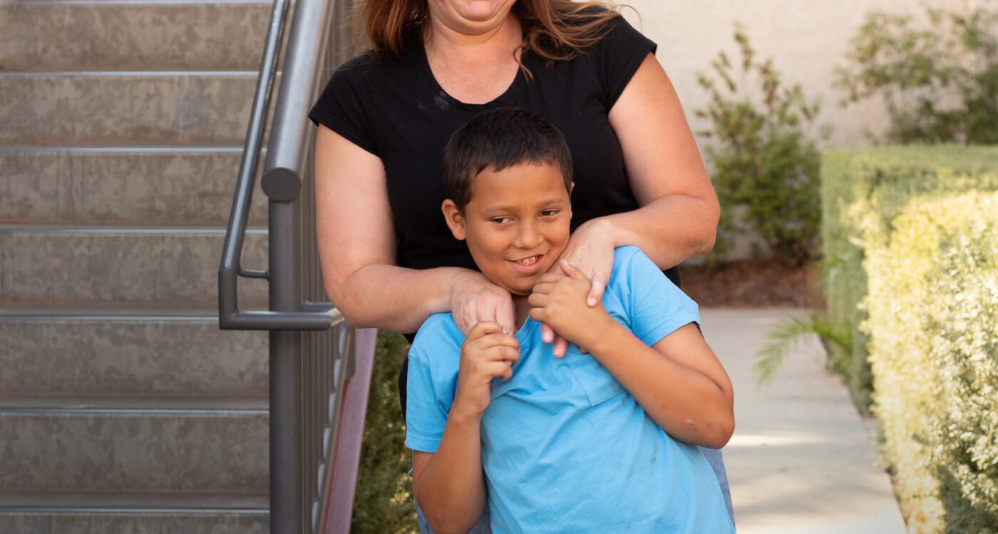 A mom stands behind her son next to a staircase