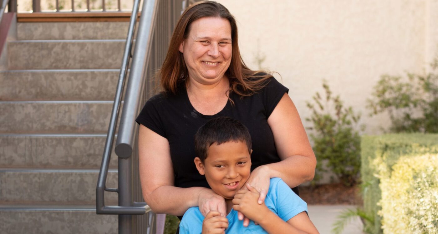 A mom stands behind her son next to a staircase