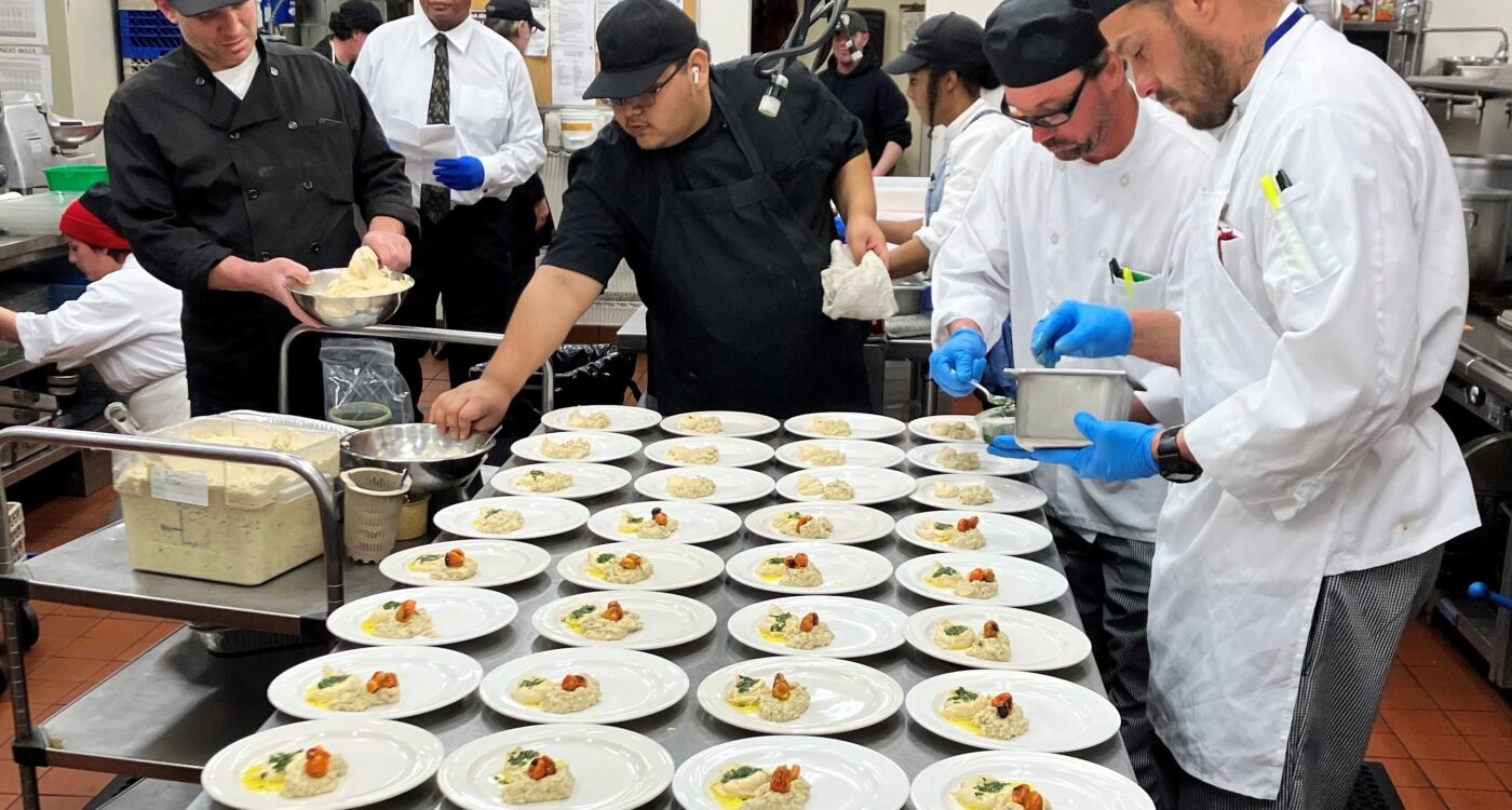 Student chefs put food on a counter full of plates