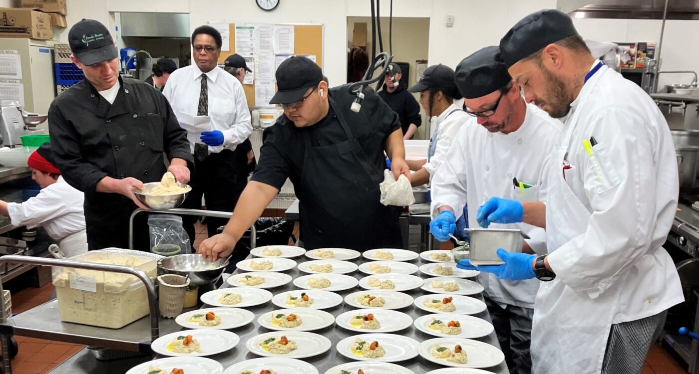 Student chefs put food on a counter full of plates