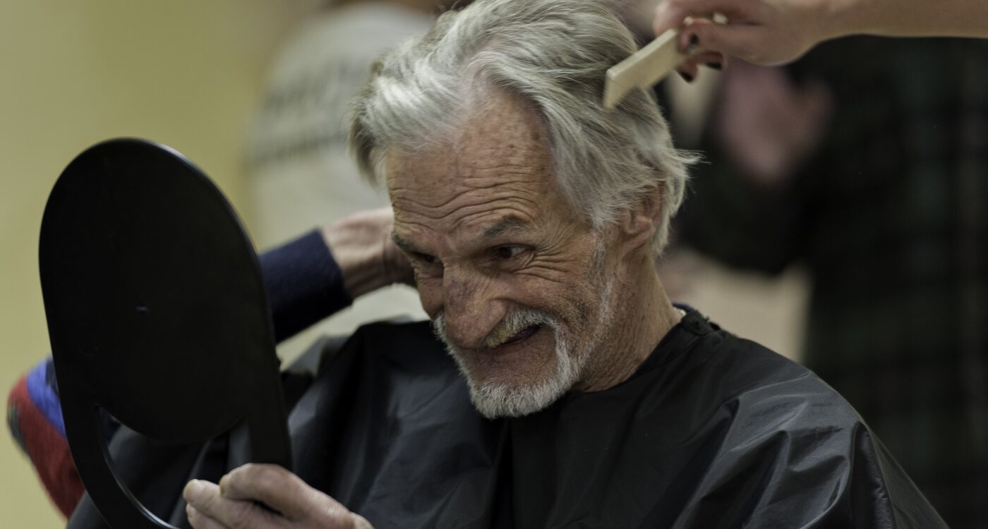 A man smiles to himself in the mirror as his hair is being cut