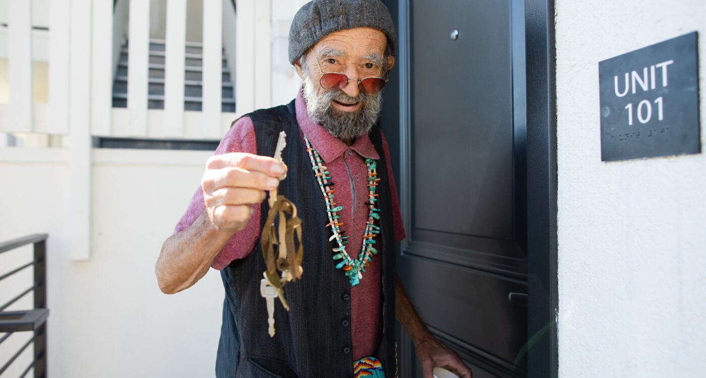 A man holding up a key at a door outside of La Casa Buena