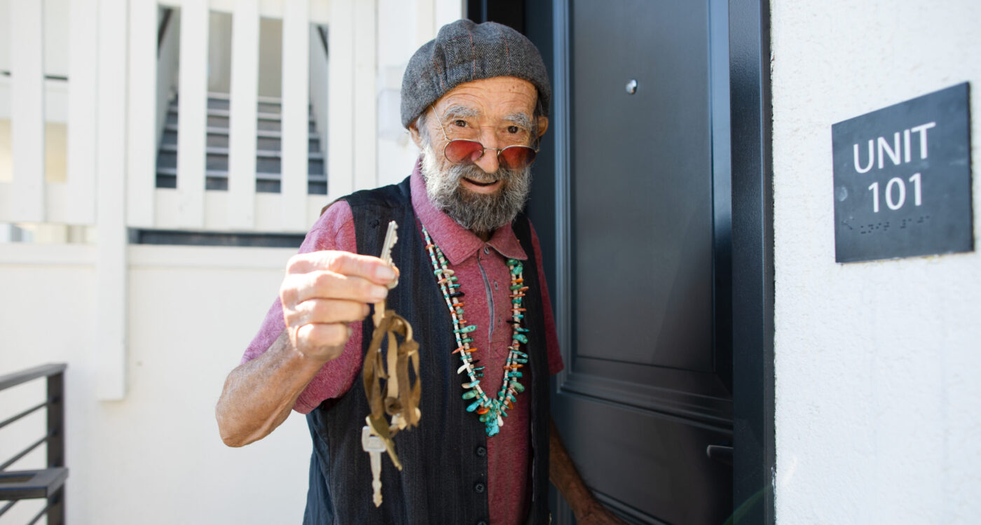 A man holding up a key at a door outside of La Casa Buena