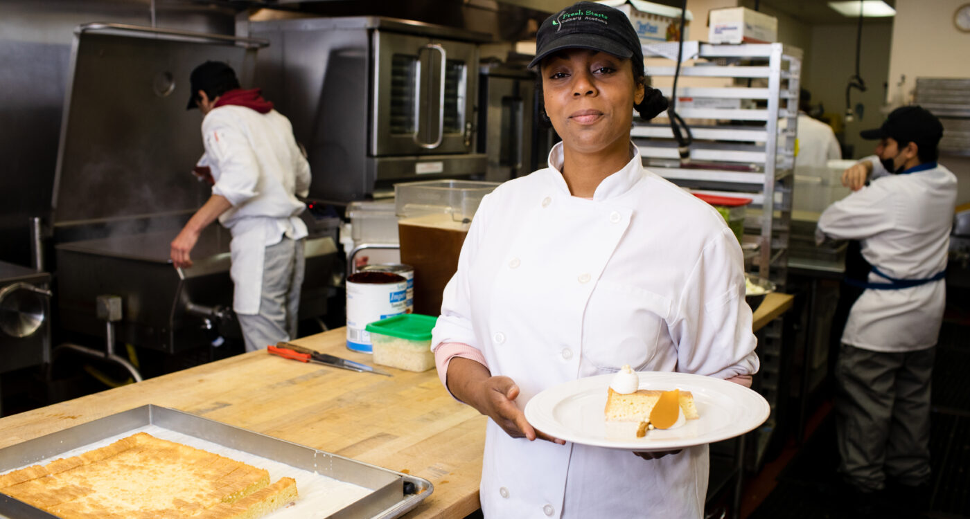 A Fresh Starts Culinary Academy student holds a plate with a slice of cake on it