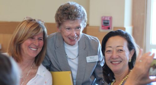 Three women gather around a dining table to pose for a photo.