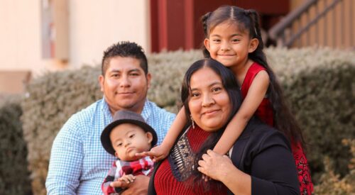 Man in blue shirt and woman in black sweater hold their children, a baby boy and a school-age girl with long dark hair.