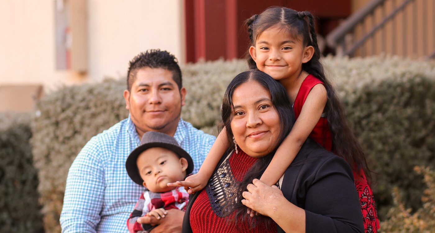 Man in blue shirt and woman in black sweater hold their children, a baby boy and a school-age girl with long dark hair.