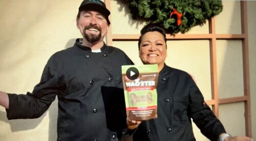 Man and woman in black chef coats smile at the camera. The woman holds a bag of Wagster Treats