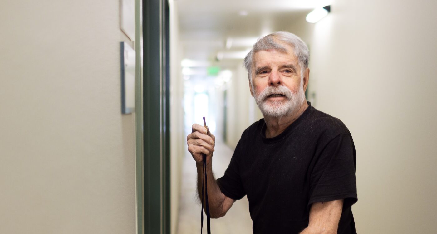 Man with gray hair and black T-shirt holds up key near apartment door.