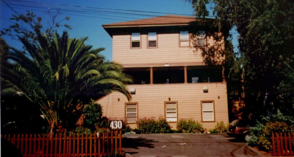 Two story brown home with front porch under eaves.