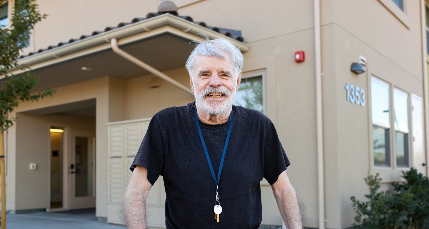 Man with white hair and beard smiles at the camera. He is wearing a lanyard of keys around his neck.