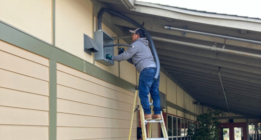 Man on ladder works at side of New Beginnings Center shelter.