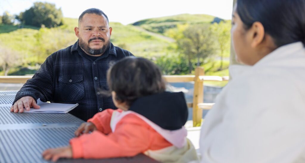 Man wearing plaid shirt sits at picnic table with mom and young girl