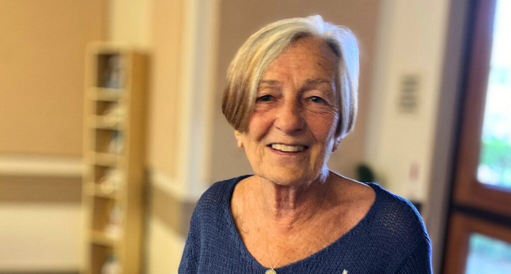 Woman with short graying hair and blue sweater smiles at the camera.