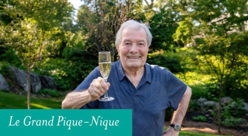 Man standing in a garden lifts glass of champagne.