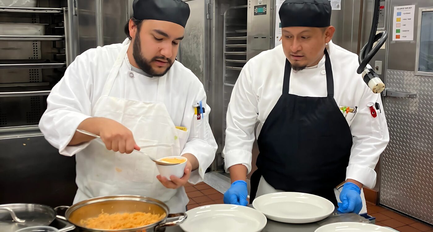 Two men in chef coats and aprons work in kitchen