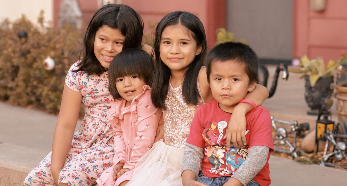 four children sit on a wall in front of a Homeward Bound apartment.
