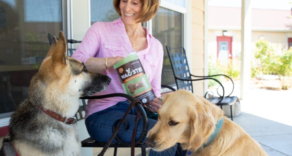 Woman wearing pink shirt sits with German shepherd dog and reaches into a bag of Wagster Treats
