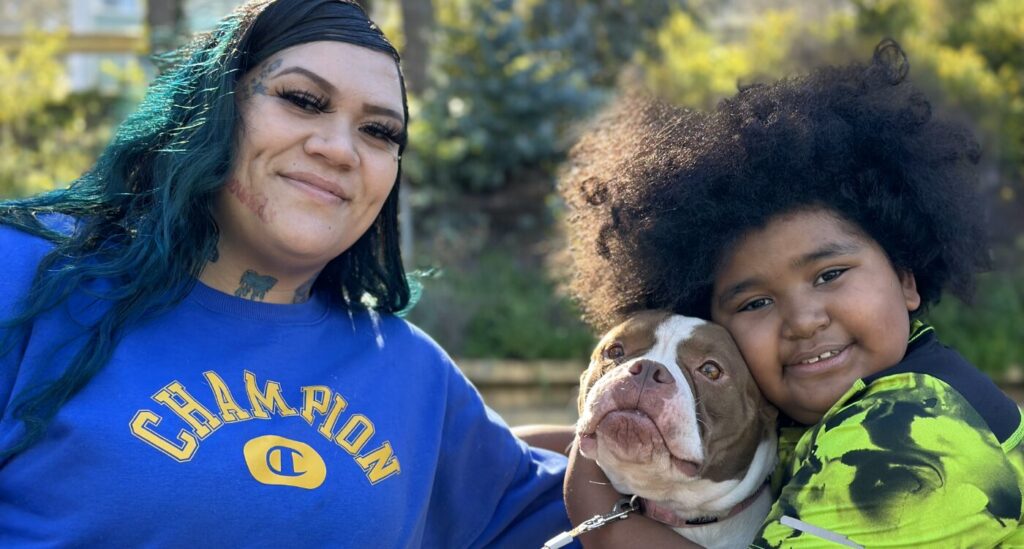 Dark-haired mom sits with son and their dog