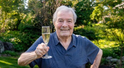 White-haired man in blue shirt holds glass of champagne