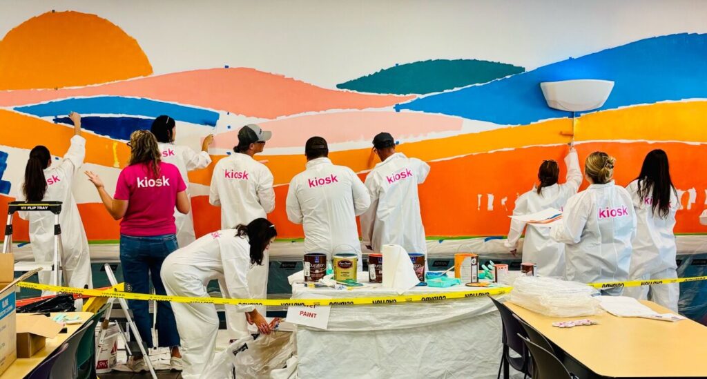People in white coveralls stand with back to camera while painting bright colors on a wall