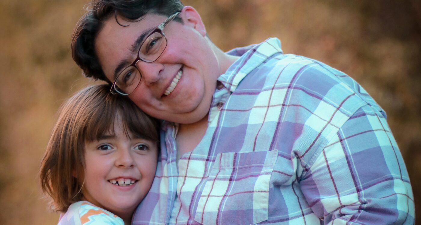 Woman with short dark hair and glasses hugs smiling daughter