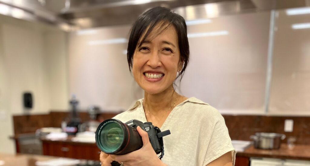 Woman with dark hair smiles as she holds camera
