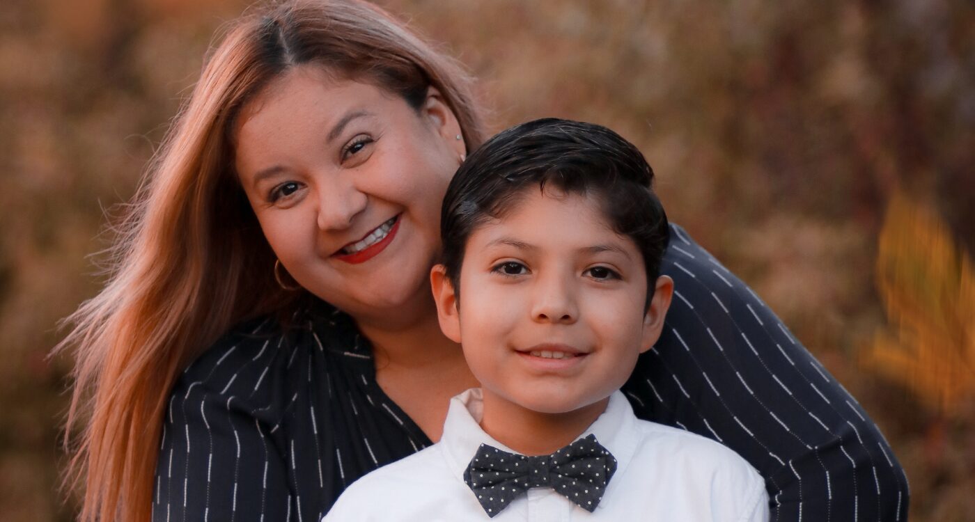 Woman with long brown hair embraces boy with white shirt and bow tie