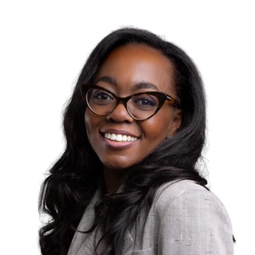 Black woman with glasses and gray blazer smiles at the camera
