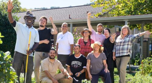 Group wearing sunhats and carrying garden tools waves while standing in the garden