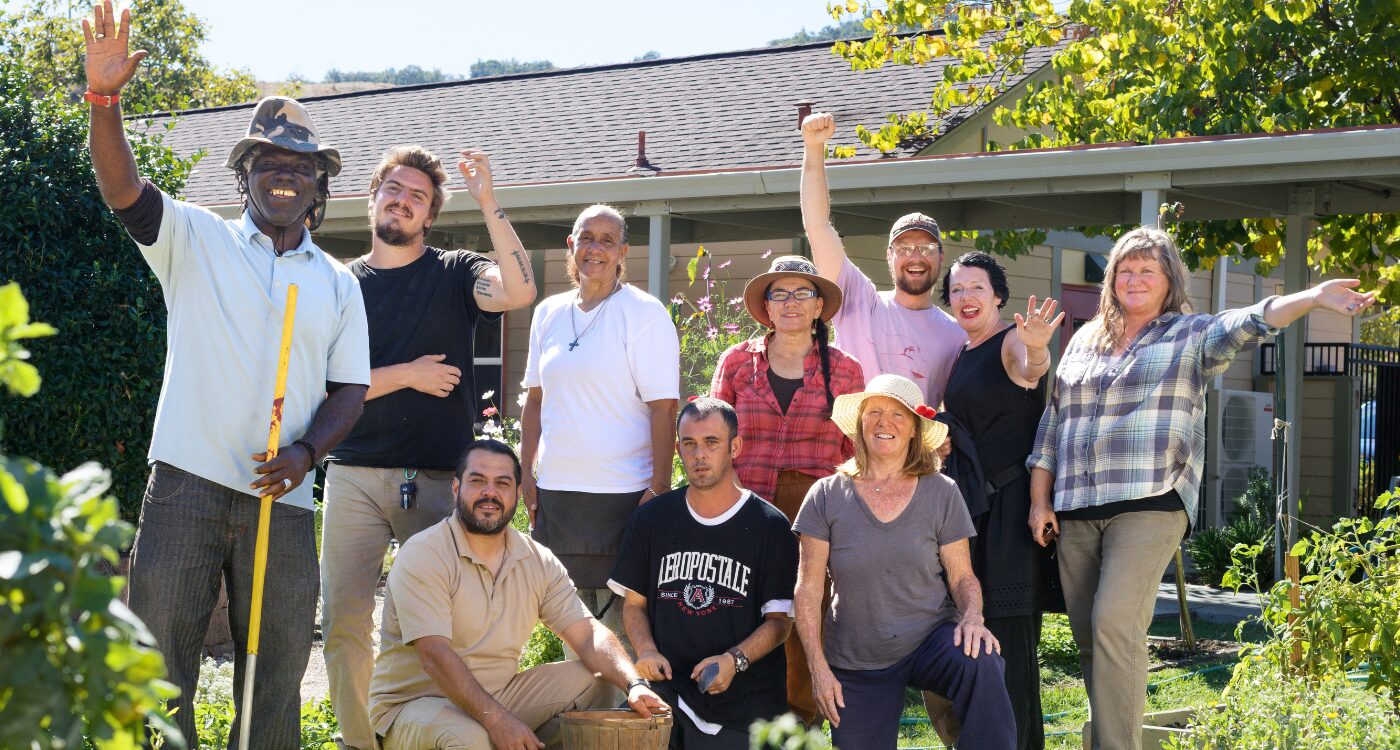 Group wearing sunhats and carrying garden tools waves while standing in the garden